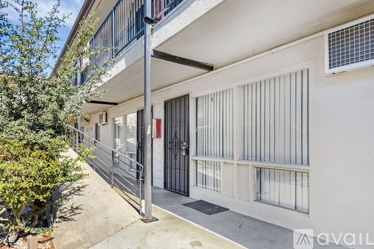 A white building with a black gate and a tree in front.