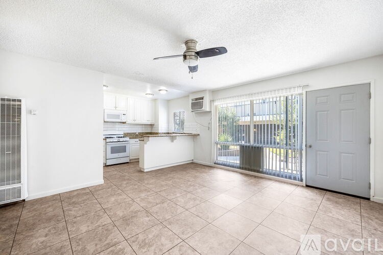 A spacious living room with a kitchen in the background and a sliding glass door leading to a balcony.