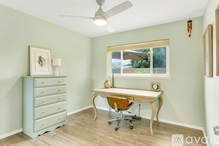 A room with a light blue dresser, a wooden desk with a chair, and a window.