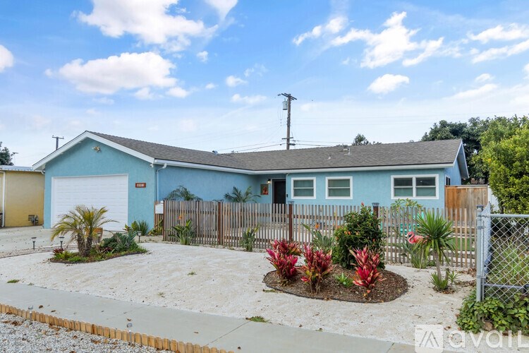 A blue house with a grey roof and a fence surrounding it.