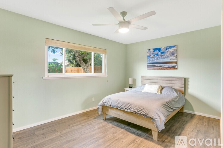 A bedroom with a bed, a ceiling fan, and a painting on the wall.