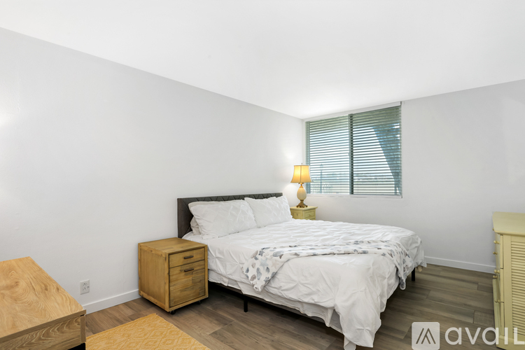 A bedroom with a bed, nightstand, and window with blinds.