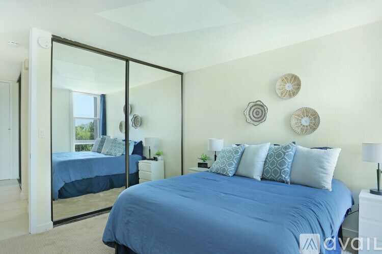 A bedroom with a blue bedspread and a mirrored wardrobe.