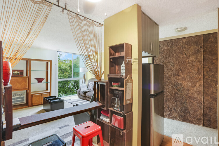 A kitchen area with a refrigerator, microwave, and a table with a red stool.