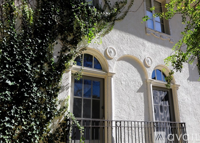 A white building with two arched windows covered in greenery.