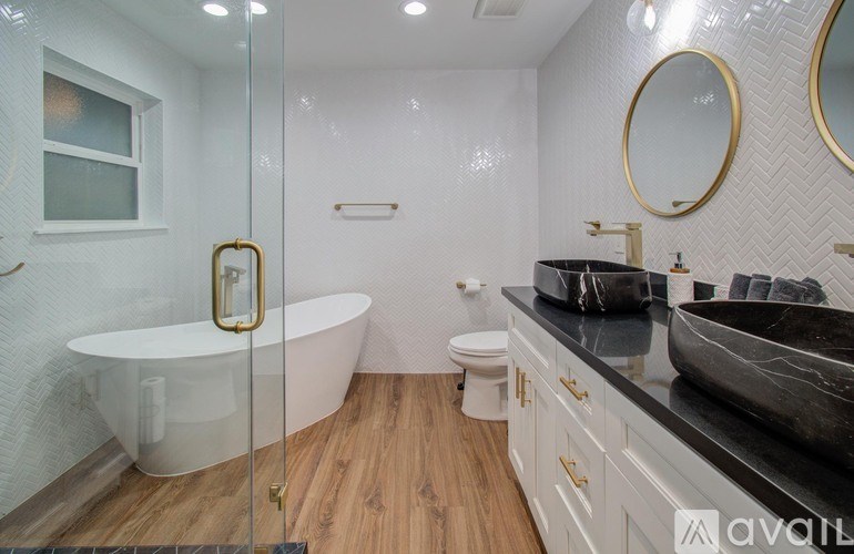 A bathroom with a white tub, black countertops, and a wooden floor.