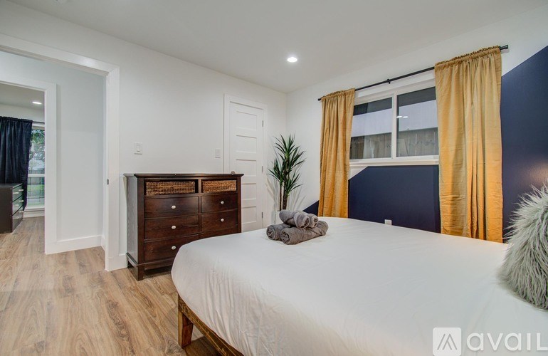 A bedroom with a white bed, wooden dresser, and a window with yellow curtains.
