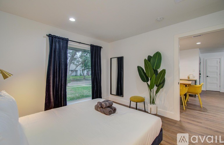 A bedroom with a large bed, a mirror, a window with curtains, and a yellow chair.