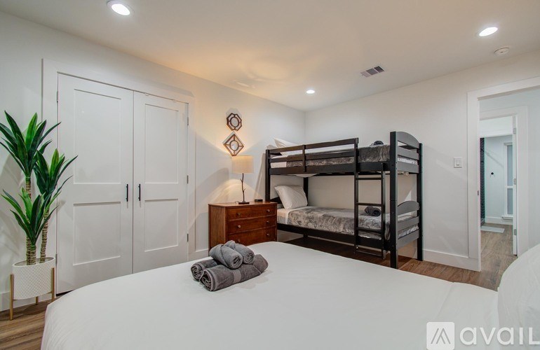 A bedroom with a white bed, a wooden dresser, and a bunk bed.