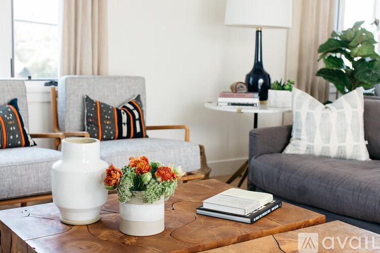 A living room with a grey couch, a wooden table with a vase and a book on it, and a lamp in the background.