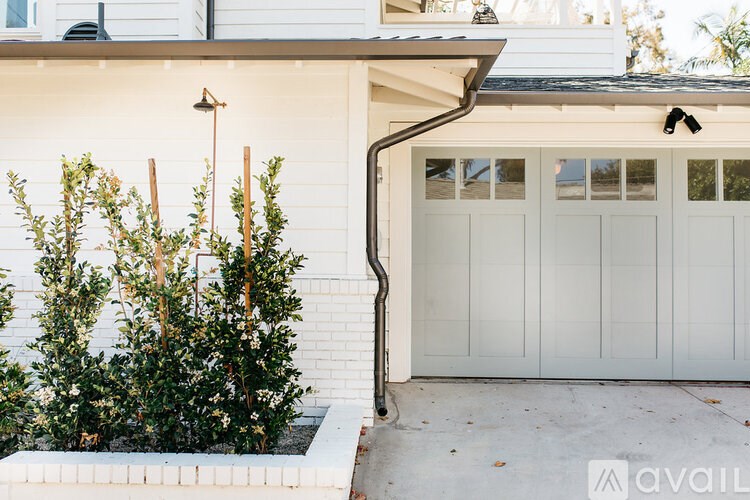 A white house with a grey garage door and a small garden in front.