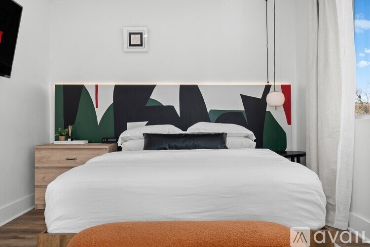 A bedroom with a white bed and a wall hanging with black and red shapes.