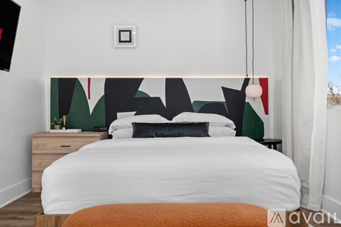 A bedroom with a white bed and a wall hanging with black and red shapes.