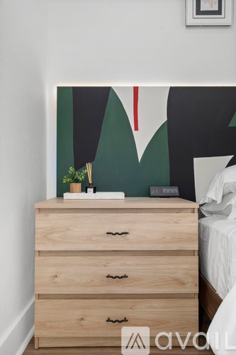 A wooden chest of drawers with a plant on top and a picture on the wall.
