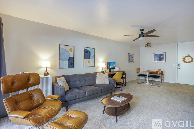 A living room with a grey couch, two brown leather chairs, a coffee table, and a ceiling fan.