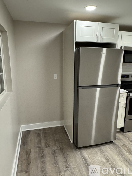 A stainless steel refrigerator in a kitchen with wooden flooring.