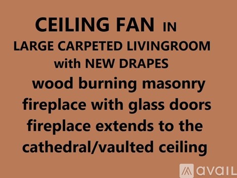 Ceiling fan in a large carpeted living room with new drapes and a wood burning masonry fireplace with glass doors.