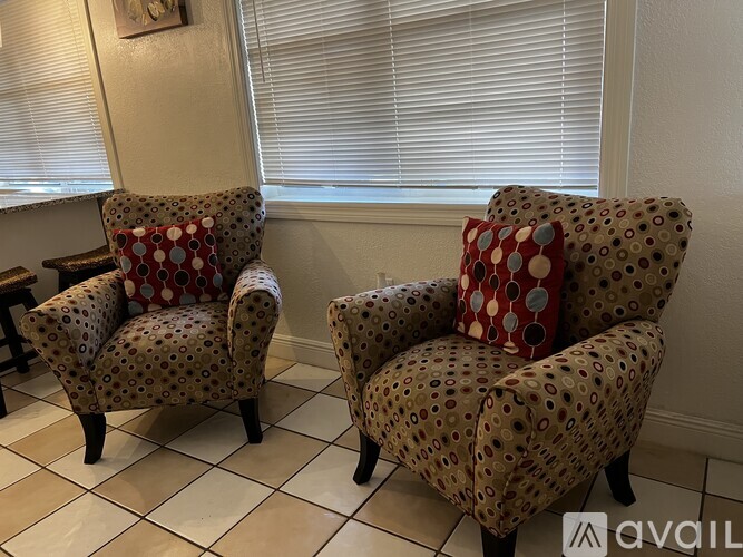 Two chairs with red and white pillows are in front of a window.
