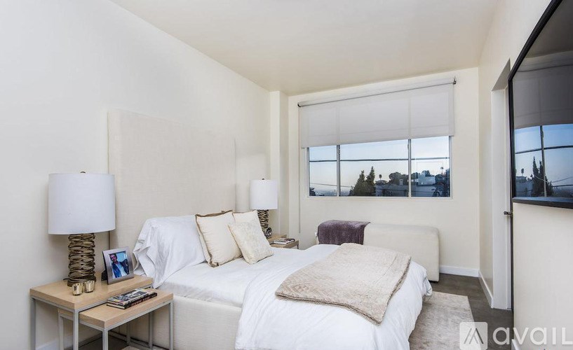A bedroom with a large bed, a nightstand with a lamp, and a window with a view of trees.