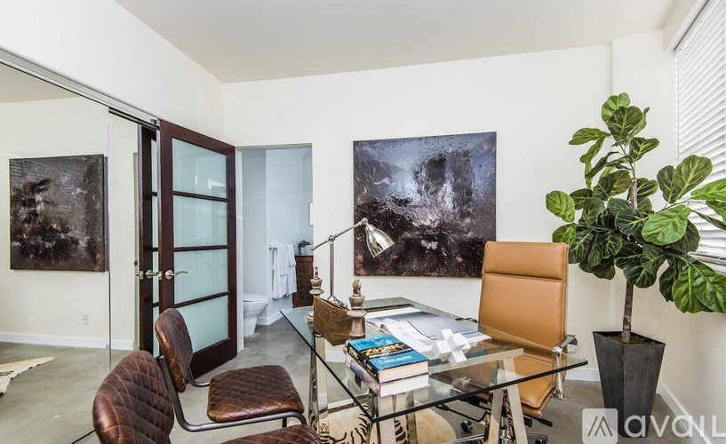 A room with a glass table and chairs, a potted plant, and two posters on the wall.