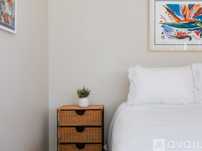 A white bed with a white pillow and a brown drawer with a plant on top.
