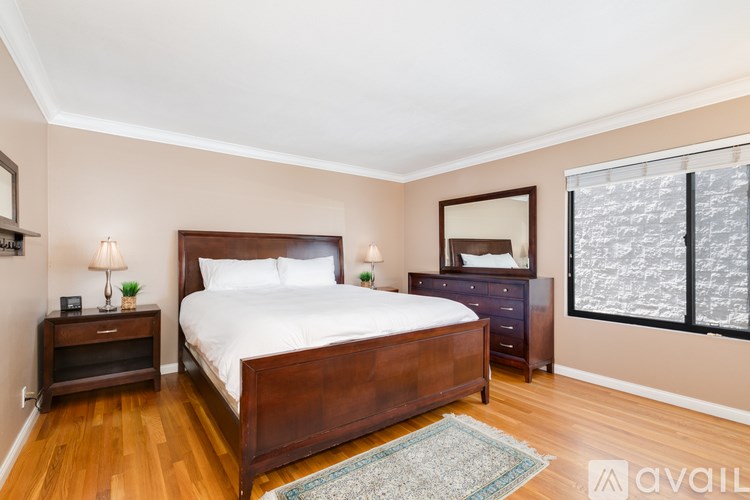 A bedroom with a large bed, a nightstand, and a window with blinds.