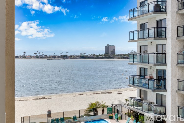 A view of a beach from a balcony with a pool and palm trees in the distance.