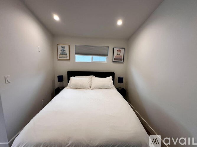 A bedroom with a white bed and two pictures on the wall.