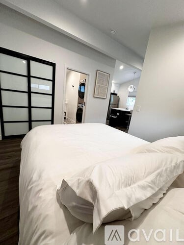 A bed with white sheets and pillows in a room with a wooden floor.