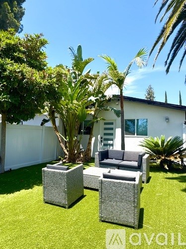 A white house with a patio and a tree in front.