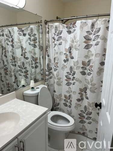 A bathroom with a sink, toilet and a shower curtain with leaves on it.