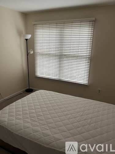A bedroom with a bed, a window with blinds, and a floor lamp.