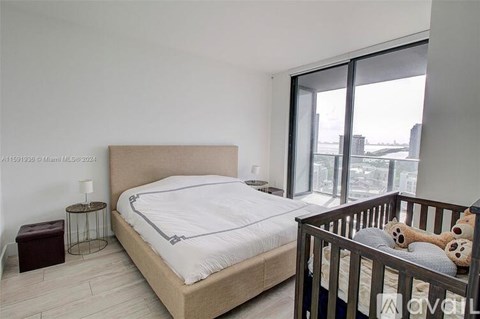 A bedroom with a large bed and a crib with a teddy bear inside.