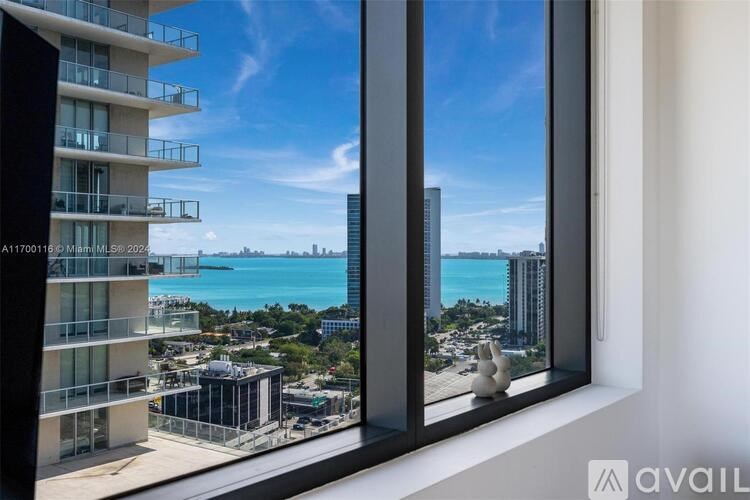 A view from a window of a balcony overlooking a cityscape and a body of water.