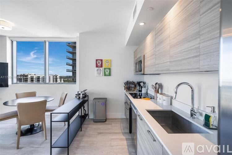 A modern kitchen with a dining table and chairs, a sink, and a window overlooking a cityscape.