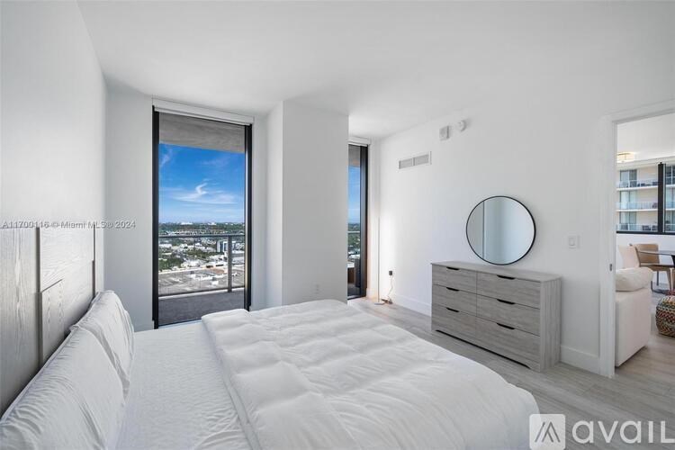 A bedroom with a large bed, a dresser, and a view of the city through the window.