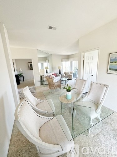 A glass table with white chairs in a spacious room.