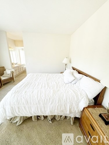 A bed with white bedding and a wooden headboard sits in a room with a carpeted floor.
