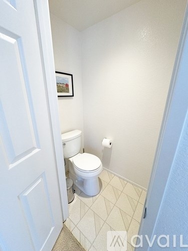 A white toilet in a small bathroom with a white door and a picture on the wall.