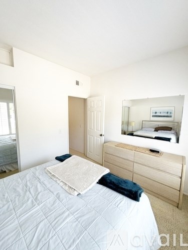 A bedroom with a bed, dresser, mirror, and window.