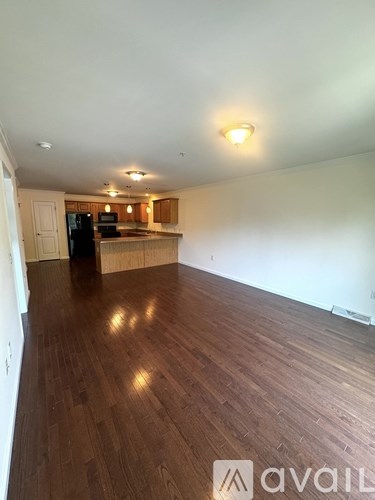 A room with wooden floors and a kitchen area in the background.