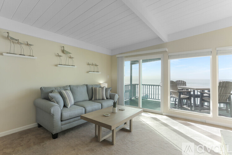 A living room with a grey couch and a glass door leading to a balcony.