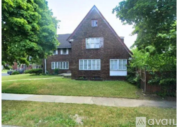 A house with a brown brick exterior and white trim is surrounded by greenery.