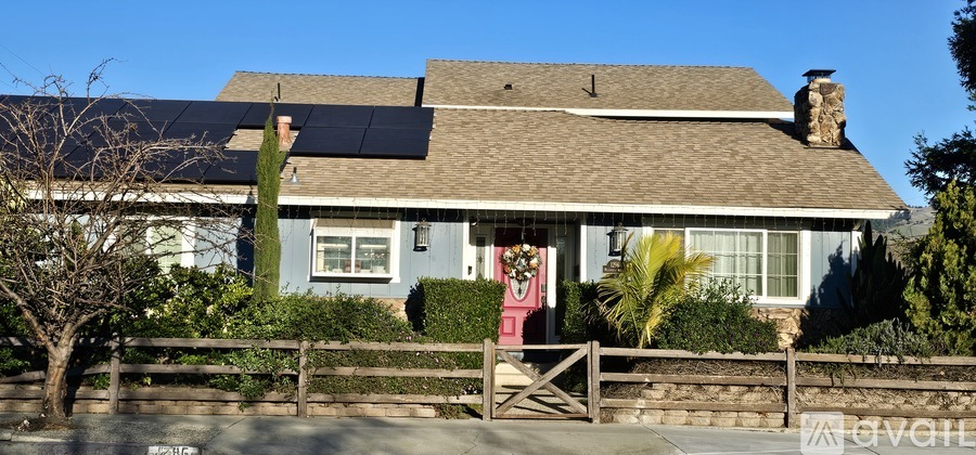 A house with solar panels on the roof and a fence in front.