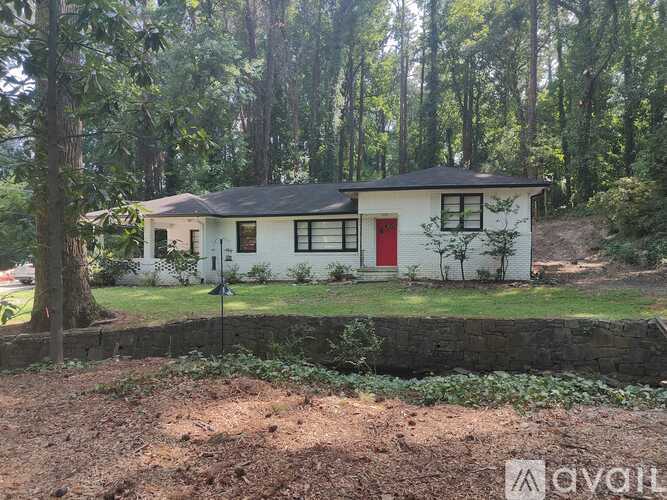 A white house with a red door is surrounded by trees.