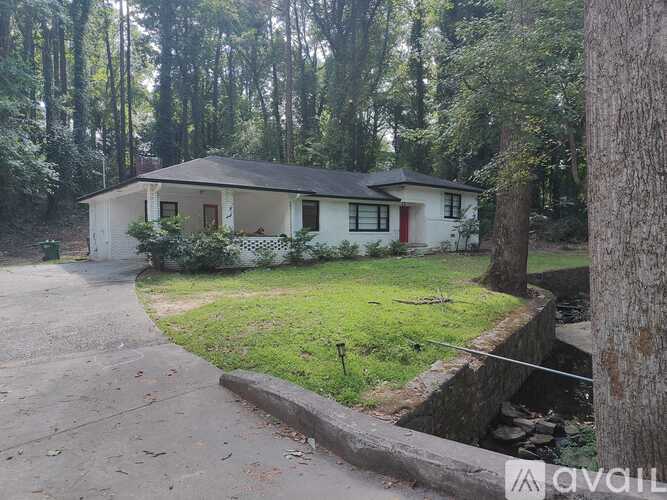 A house with a white exterior and a red door is surrounded by a forest.