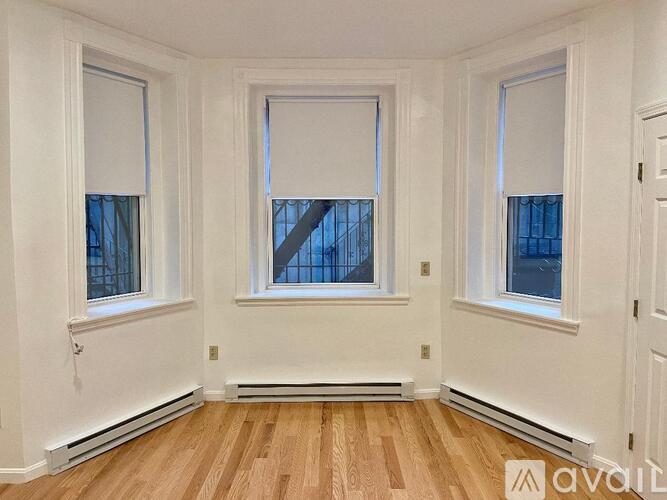 A room with white walls and wooden flooring, featuring two windows with blinds.