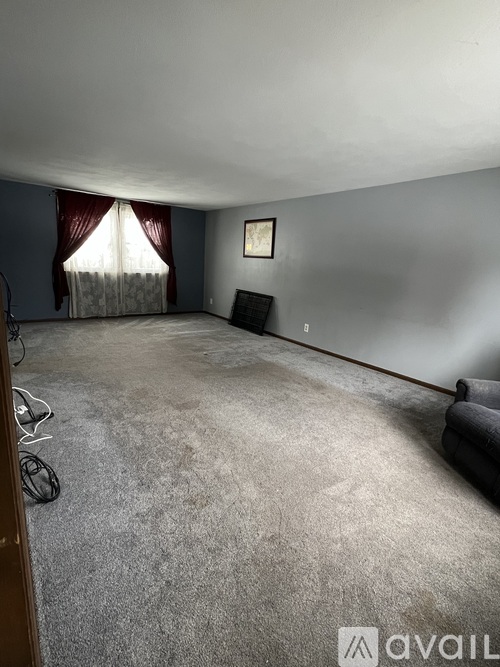 A room with a grey carpet and a window with red curtains.
