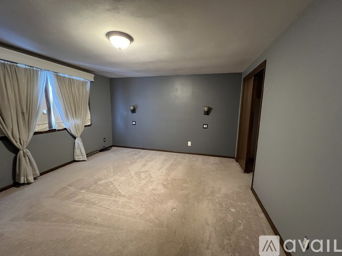A room with a carpeted floor and a window with curtains.