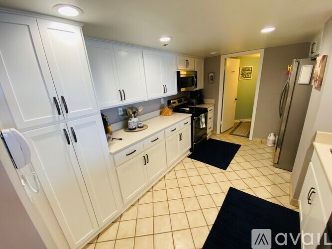 A kitchen with white cabinets and appliances, a black mat on the floor, and a door to a green room.